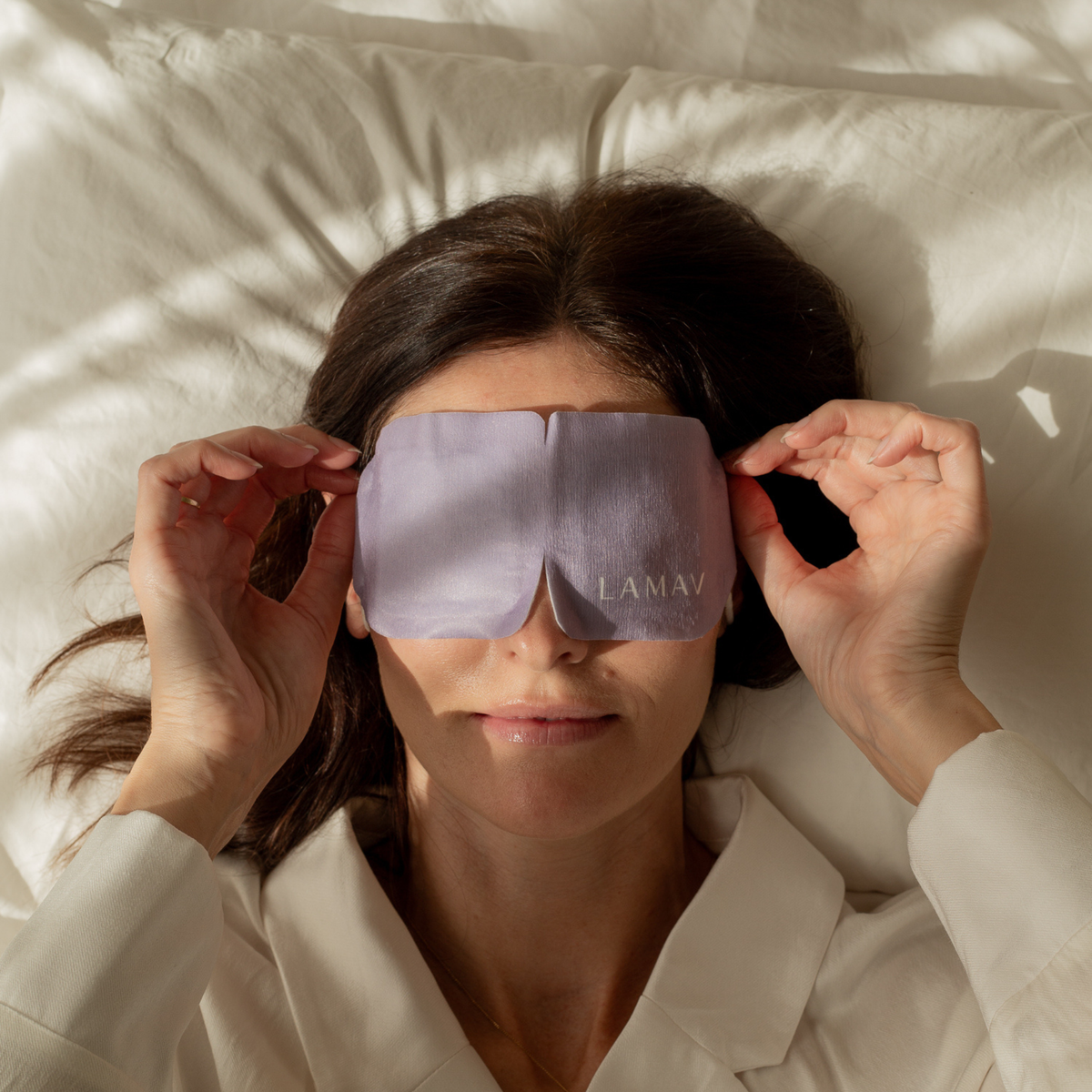 Woman relaxing in bed wearing a LAMAV warm eye mask for sleep